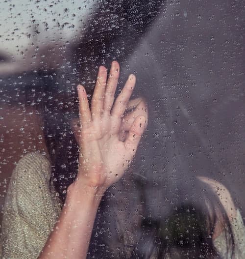 Hand an regennasser Scheibe, dahinter eine Person